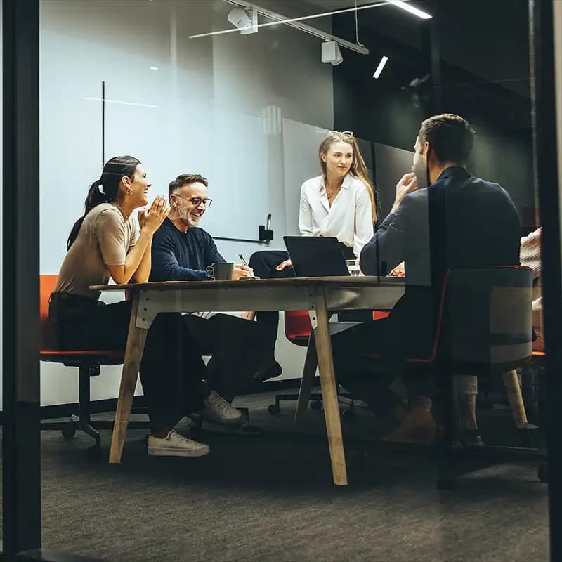 Team-Meeting in einem modernen Konferenzraum mit klaren Glaswänden, das Zusammenarbeit und Diskussion zeigt.